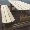 Wooden picnic bench with rounded edges and H-frame design beside an outdoors tennis court
