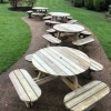 Row of four traditional round park style picnic benches with rounded seats and umbrella holes