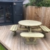 Traditional round picnic table with rounded seats and umbrella hole on garden decking next to summerhouse