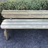 Classic park style wooden bench with rounded edges and back rest on stone floor near flower beds